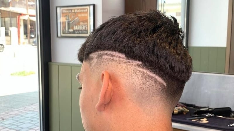 Κούρεμα skin fade με χαραγμένη γραμμή στο πλάι, από πίσω, μπροστά στη βιτρίνα του μαγαζιού